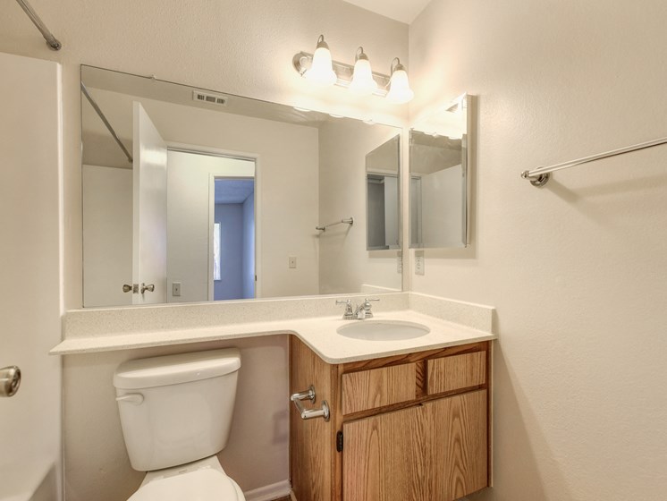 Vacant apartment home bathroom with sink and vanity.  Large mirror and bright lighting above the sink.